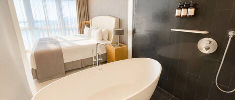 A modern bathroom with a freestanding bathtub, a shower area, and a bedside table with toiletries.