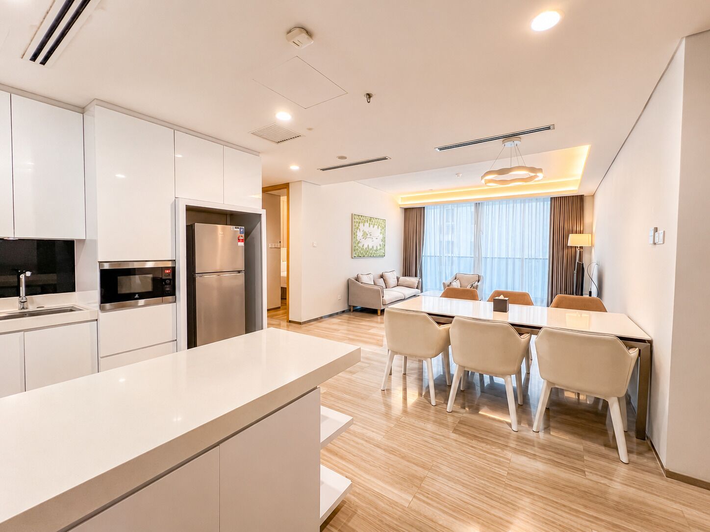 A modern kitchen with a refrigerator, microwave, and sink. There is a dining area with a table and chairs.