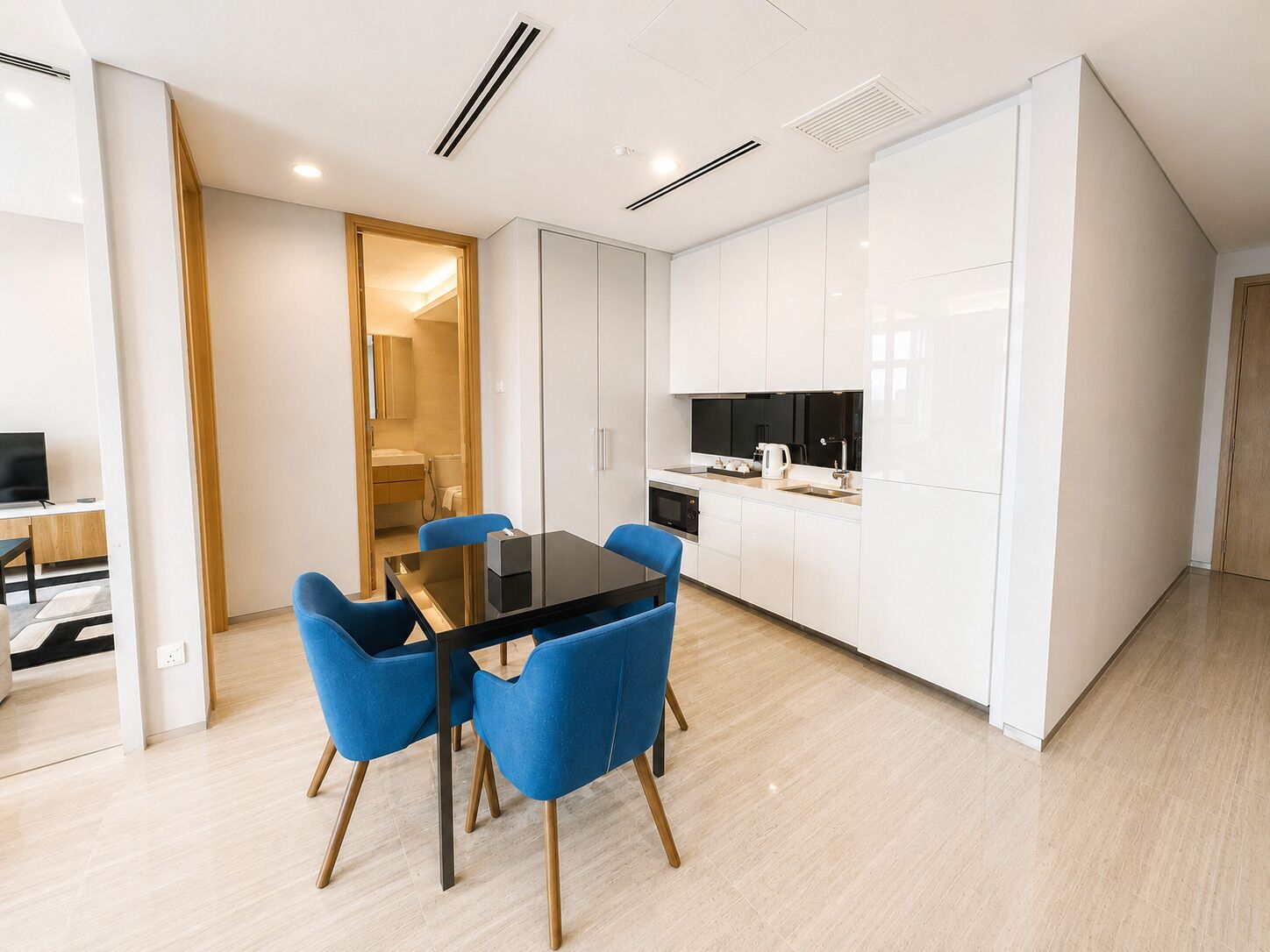 A modern kitchen with white cabinets, a black countertop, and a microwave. There is a dining area with a black table and blue chairs.
