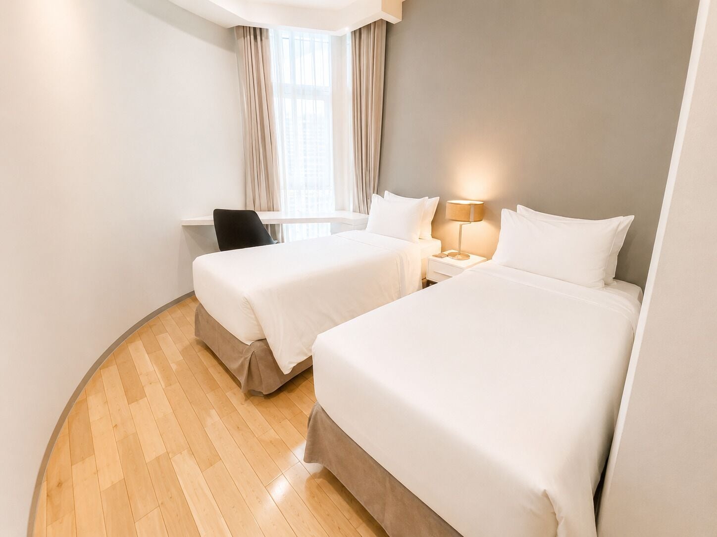 Une chambre d’hôtel avec deux lits, un bureau, une chaise et une fenêtre avec des rideaux.