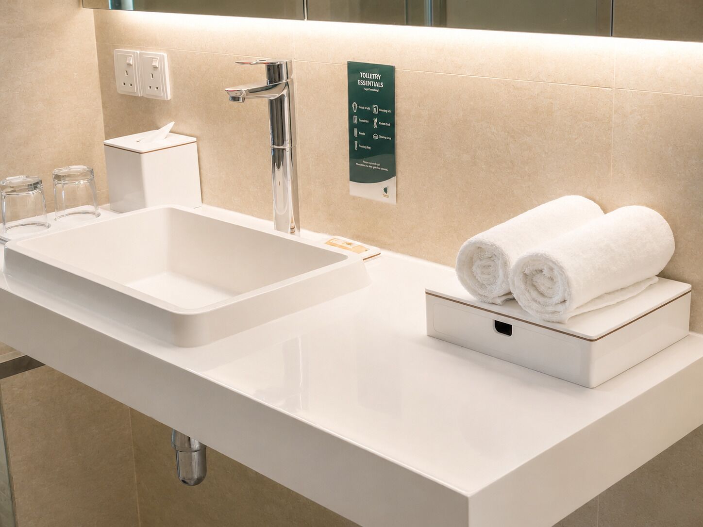 Un baño moderno con un lavamanos blanco, un espejo y un dispensador de toallas.