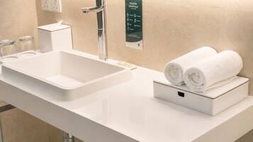 Un baño moderno con un lavamanos blanco, un espejo y un dispensador de toallas.