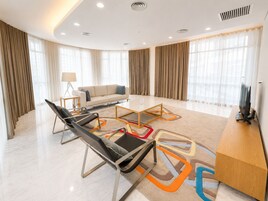 A modern hotel room with a sofa, two chairs, a TV, and a desk.