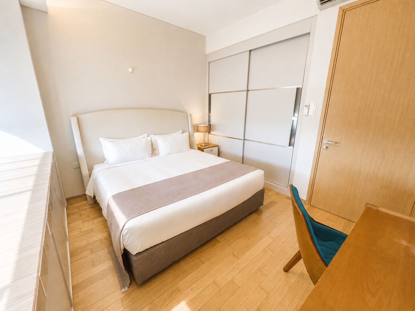 Une chambre d’hôtel avec un grand lit, une armoire, une table de chevet avec une lampe et un plancher en bois.