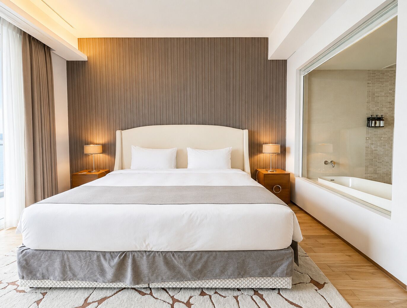 Ein Hotelzimmer mit einem großen Bett, Nachttischlampen, einem Badezimmer mit einer Badewanne und Blick auf die Stadt.