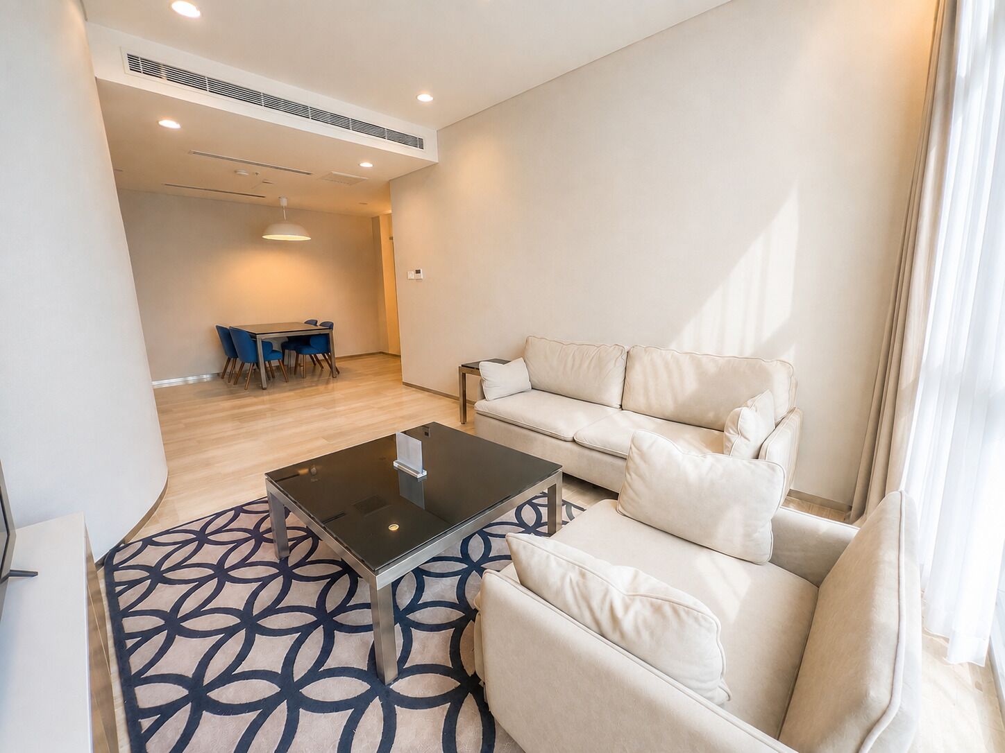 Un salon moderne avec un canapé, une table basse en verre et un tapis à motifs.