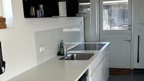 Ett modernt kök med en vit bänkskiva, en diskho i rostfritt stål och en diskmaskin. Det finns ett fönster med utsikt över omgivningen.