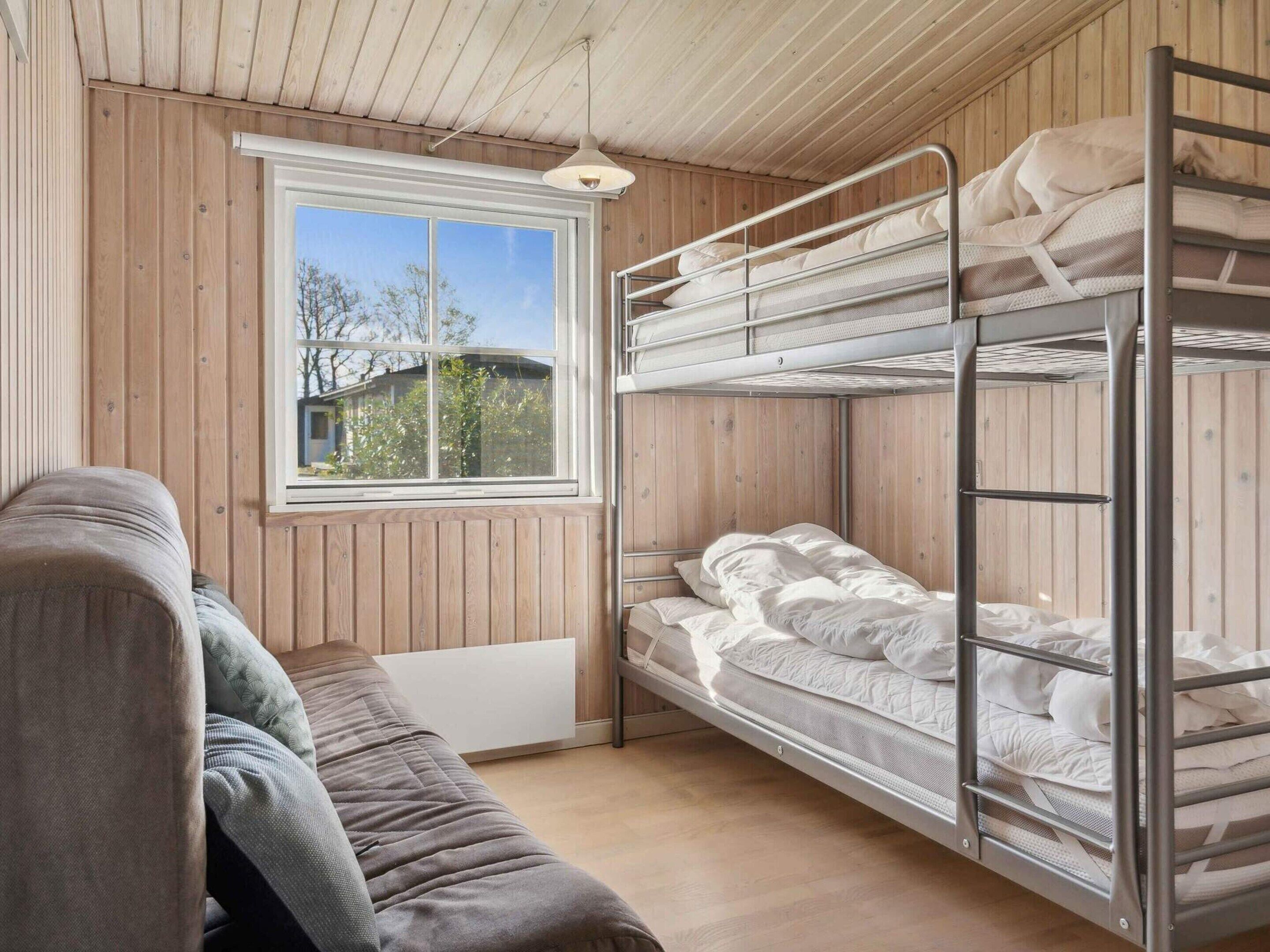 A bunk bed room with a window, a sofa, and wooden walls.