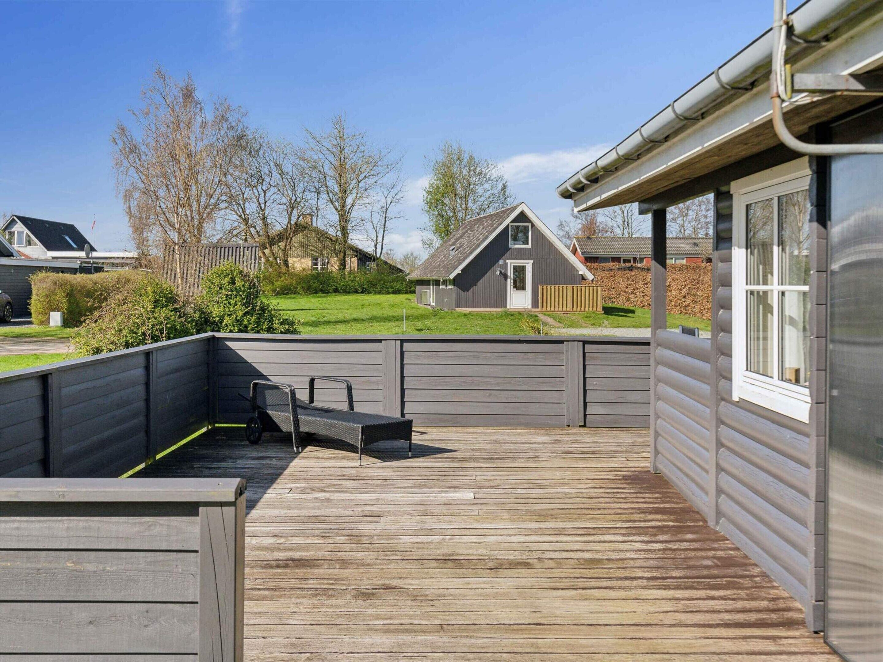 Una terraza de madera con un banco incorporado y una pequeña mesa, rodeada por una valla gris.
