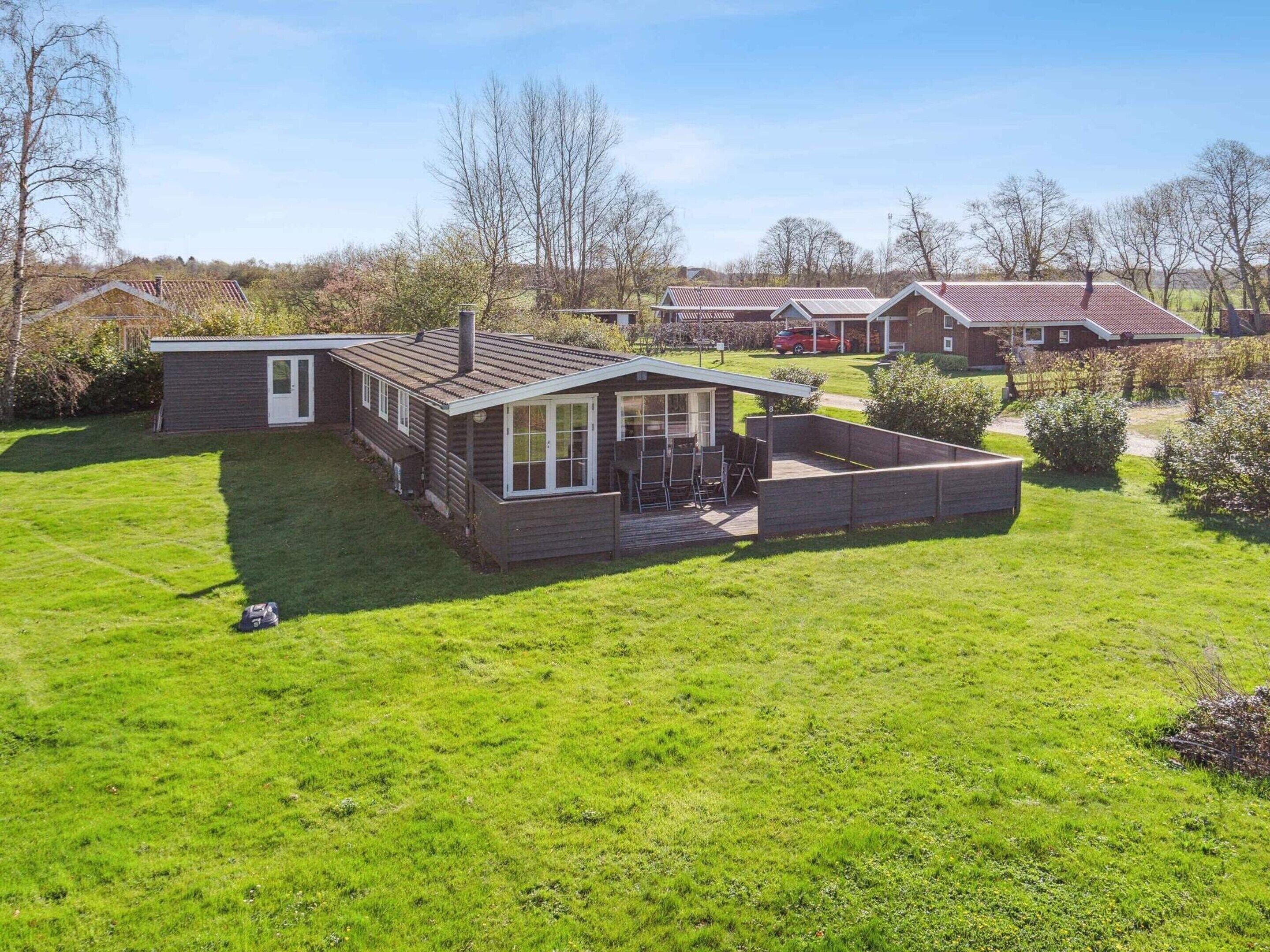 A single-story wooden house with a fenced backyard, a patio, and a car parked nearby.