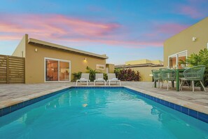 A swimming pool with lounge chairs and a table, surrounded by a patio area.