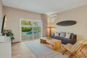 Un salon moderne avec un canapé, une table basse et des fauteuils, une vue sur la piscine et un appareil de climatisation.
