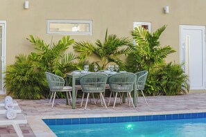 Un espace de restauration en plein air avec une piscine, entouré d’une végétation luxuriante et d’un mur de couleur beige.