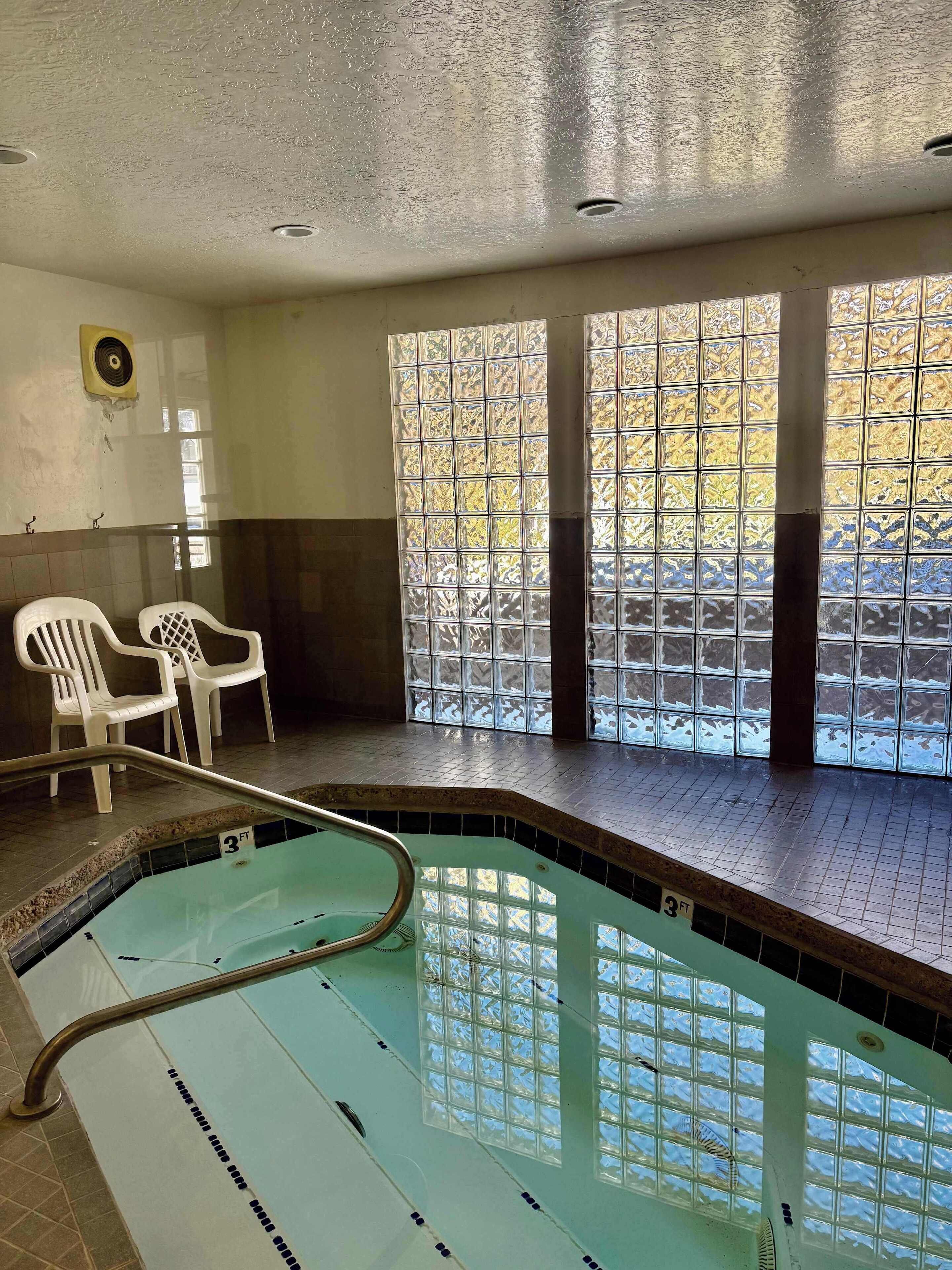An indoor swimming pool with clear water, a 3 FT depth marker, and a view through a window with patterned glass.