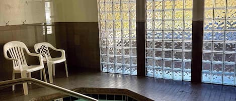 An indoor swimming pool with clear water, a 3 FT depth marker, and a view through a window with patterned glass.