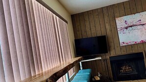 A modern living room with a wooden staircase, blue cushioned seating, a flat-screen TV, and a fireplace.
