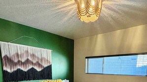 A bedroom with a bed, a wooden bench, a wall-mounted light fixture, and a window.