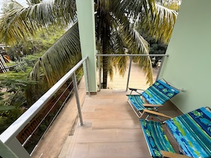 Een balkon met uitzicht op een zandstrand, omringd door palmbomen.