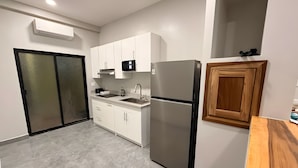 A modern kitchen with white cabinets, a stainless steel refrigerator, a microwave, and a wooden cabinet.