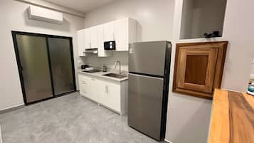 Una cocina moderna con armarios blancos, un refrigerador de acero inoxidable, un microondas y un mueble de madera.
