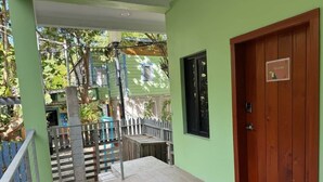 A room with a wooden door, a small table, and a view of a green building with a window. - MeMe’s Place – Toucan (Placencia)