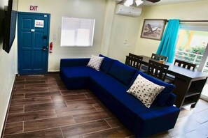 A room with a blue sofa, a dining table, and an exit door.