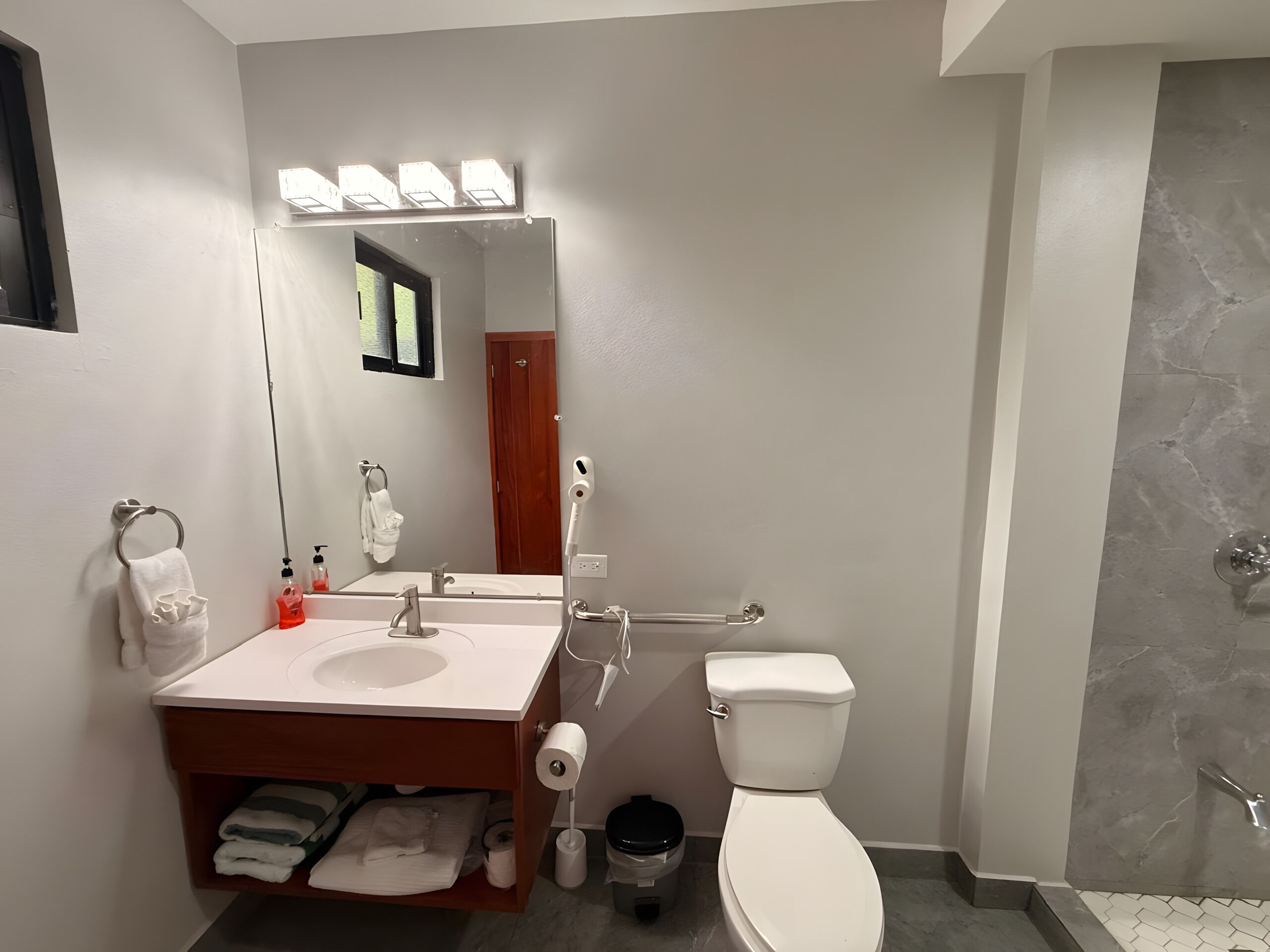 A bathroom with a vanity, sink, mirror, towel rack, toilet, and shower.