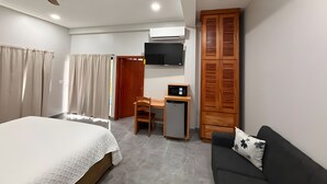 A bedroom with a bed, a desk with a chair, a TV, a wardrobe, and a sofa.