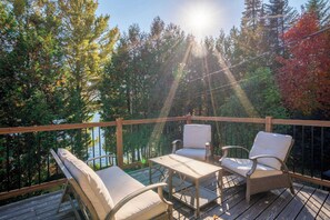 A wooden deck with two chairs and a table, overlooking a forested area and a body of water.