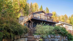 Una baita con una veranda in legno, gradini in pietra e vista sulla foresta circostante.