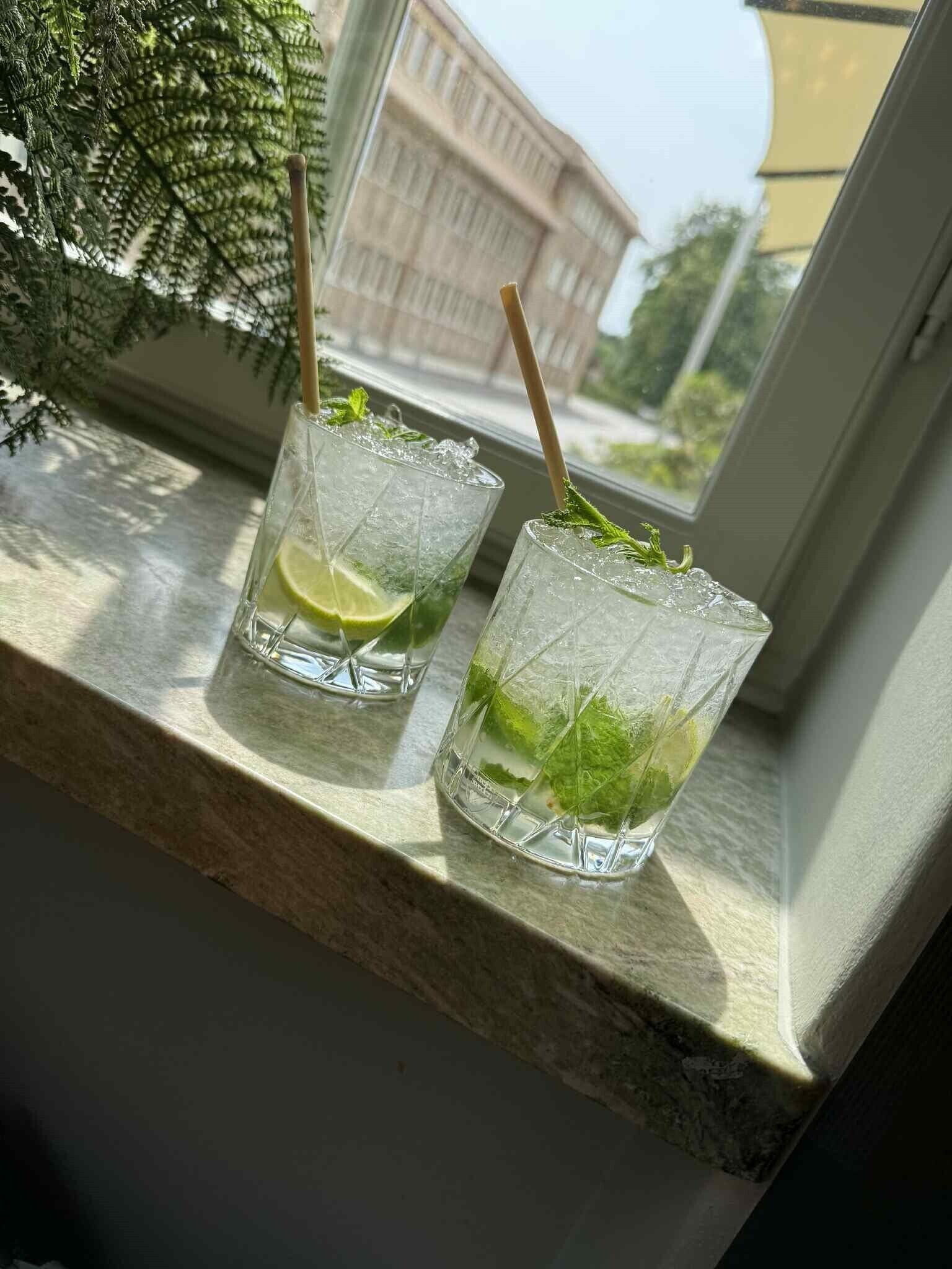 Deux verres d’une boisson au citron vert et à la menthe, posés sur un rebord de fenêtre.