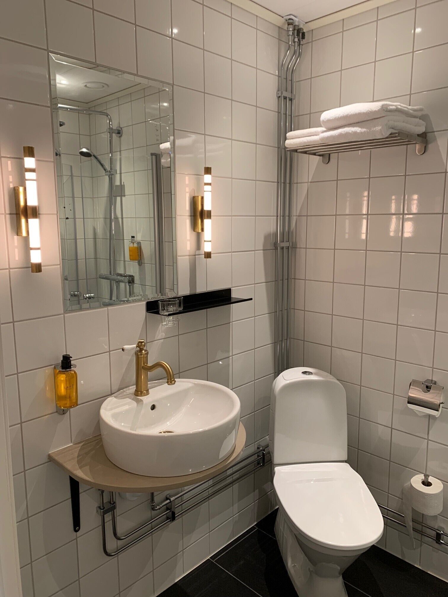 A modern bathroom with a white sink, gold faucet, and a glass shower enclosure.