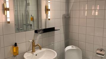 A modern bathroom with a white sink, gold faucet, and a glass shower enclosure.