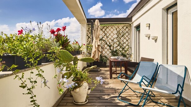 A patio with potted plants, a table, and two blue chairs. - Bright Urban Terrace | Porta Romana (Milan)