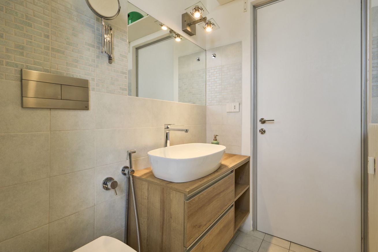 A modern bathroom with a large mirror, a vessel sink, wooden vanity, and a door.