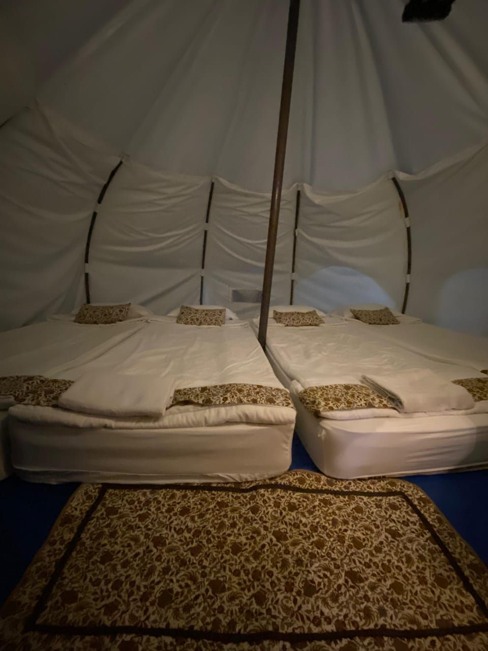 Una habitación con una cama cubierta por un dosel blanco, una alfombra estampada y un poste de madera en el centro.