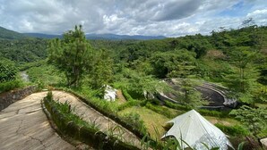 Un paysage verdoyant et luxuriant, avec un sentier sinueux, une petite construction blanche et une tente.