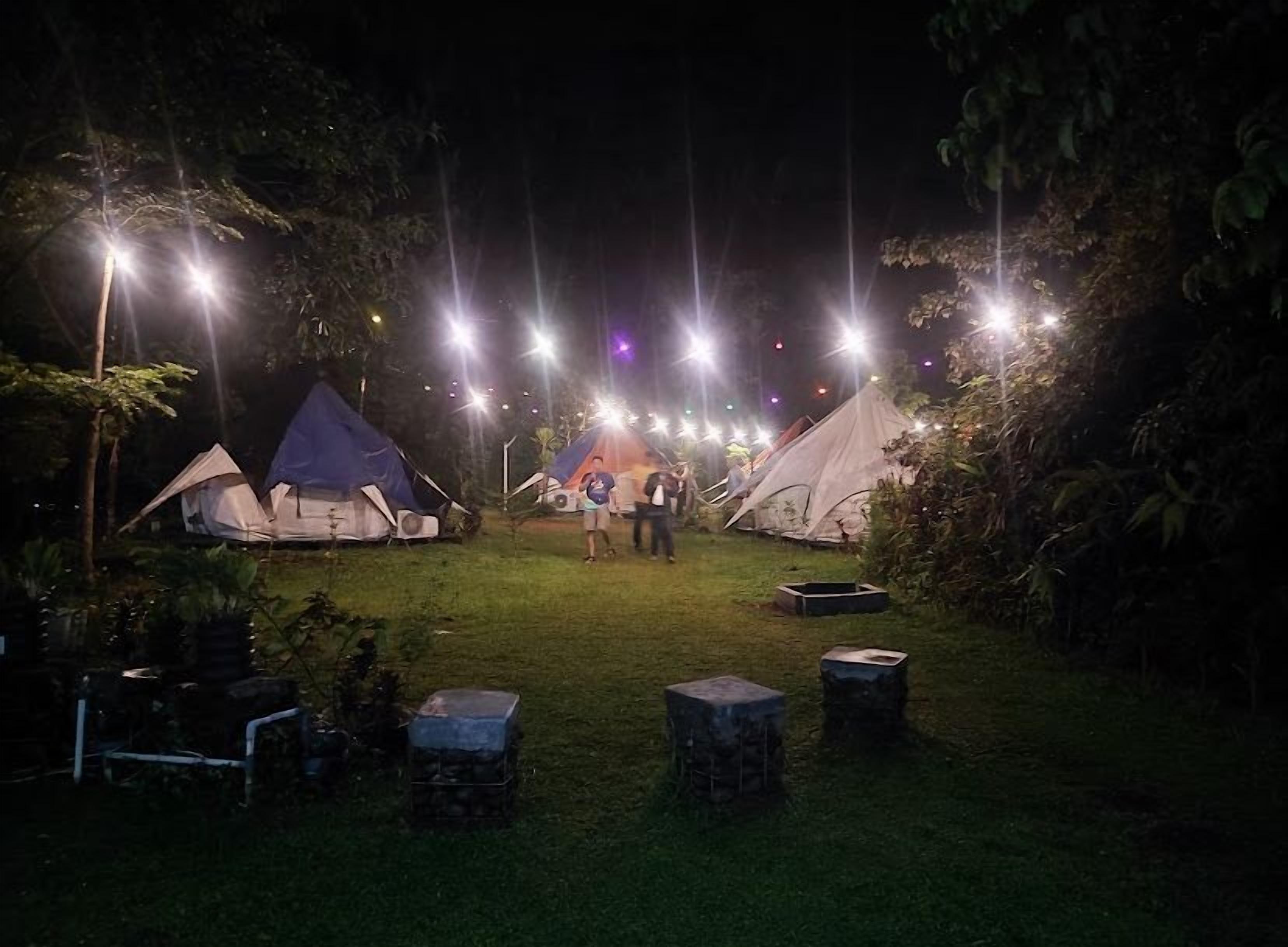 Un campamento nocturno con varias tiendas de campaña y mesas plegables.