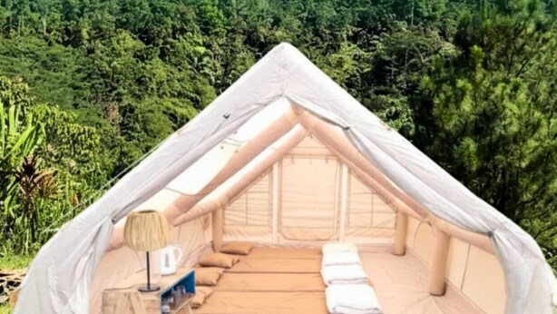 Une tente en forme de dôme, avec un lit, une petite table et une chaise à l’intérieur, entourée d’une végétation luxuriante.
