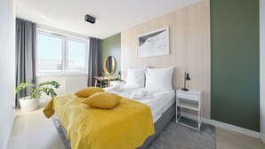 Hotelkamer met een bed, nachtkastje, bureau, stoel, een kamerplant en een raam met gordijnen.