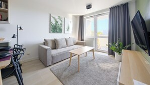 Een moderne woonkamer met een grijze bank, een houten salontafel en een groot raam met gordijnen.
