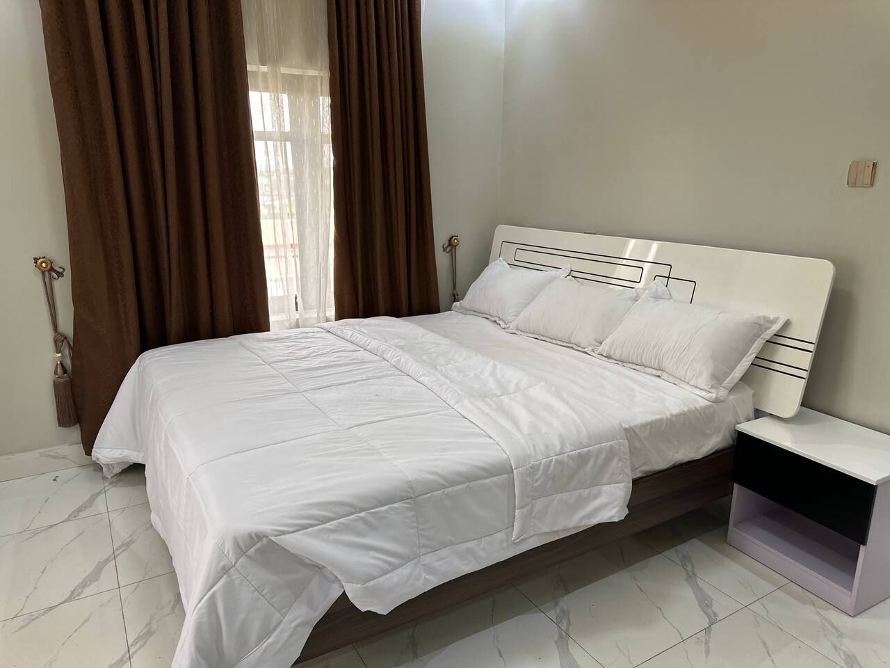 A neatly made bed with white bedding in a room with a marble floor and a white headboard.