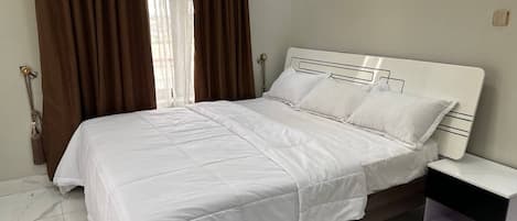 A neatly made bed with white bedding in a room with a marble floor and a white headboard.
