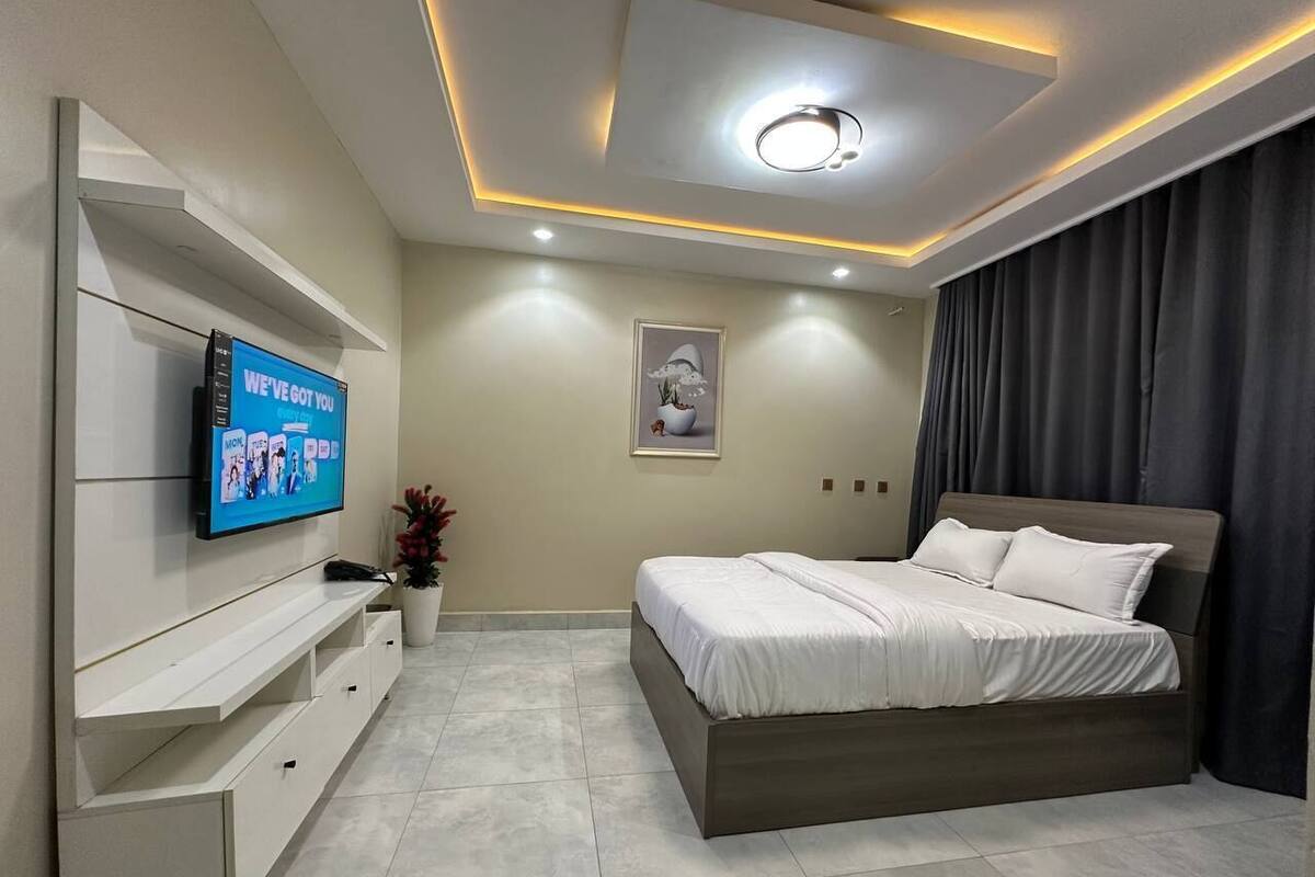 A modern bedroom with a bed, a TV mounted on a wall, and a ceiling light.