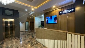 A hotel reception area with a marble floor, a reception desk, a television, and an elevator. - Prestine Apartments (Abuja)