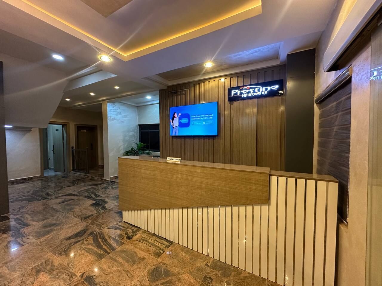 Un área de recepción con piso de mármol, un mostrador de madera, un televisor de pantalla plana y un cartel que dice 'First Relations'.