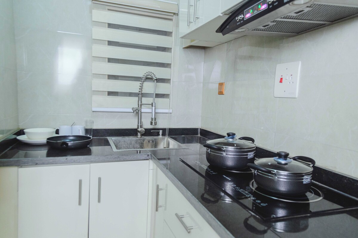 A kitchen with a black countertop, white cabinets, a stainless steel sink, and a stove with pots.
