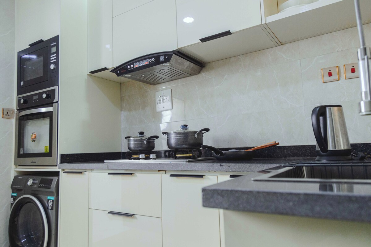 A kitchen with a microwave, oven, stove, and a kettle.