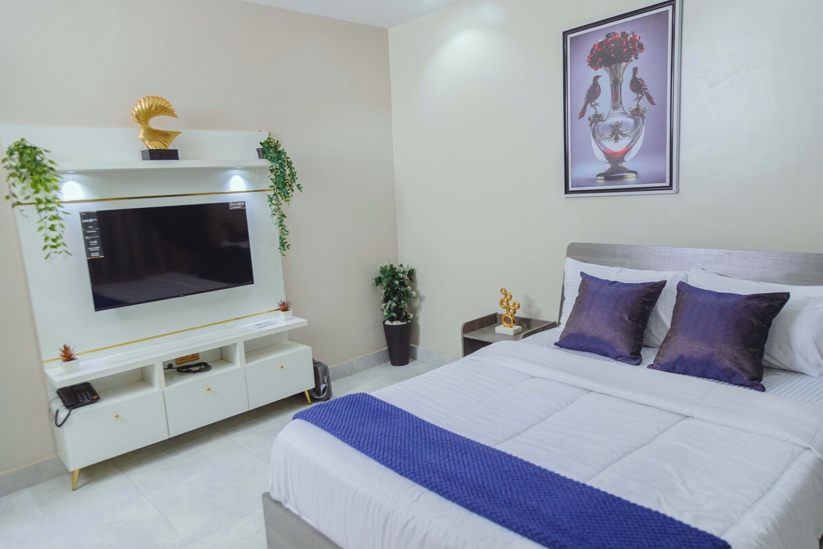A bedroom with a bed, a TV, a nightstand, and a wall-mounted painting.