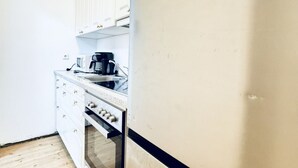 Une cuisine de taille réduite avec des meubles blancs, un évier, une machine à café et un four à micro-ondes.